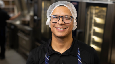 In a cozy kitchen, a cheerful man with a hat smiles, creating a friendly and inviting atmosphere.