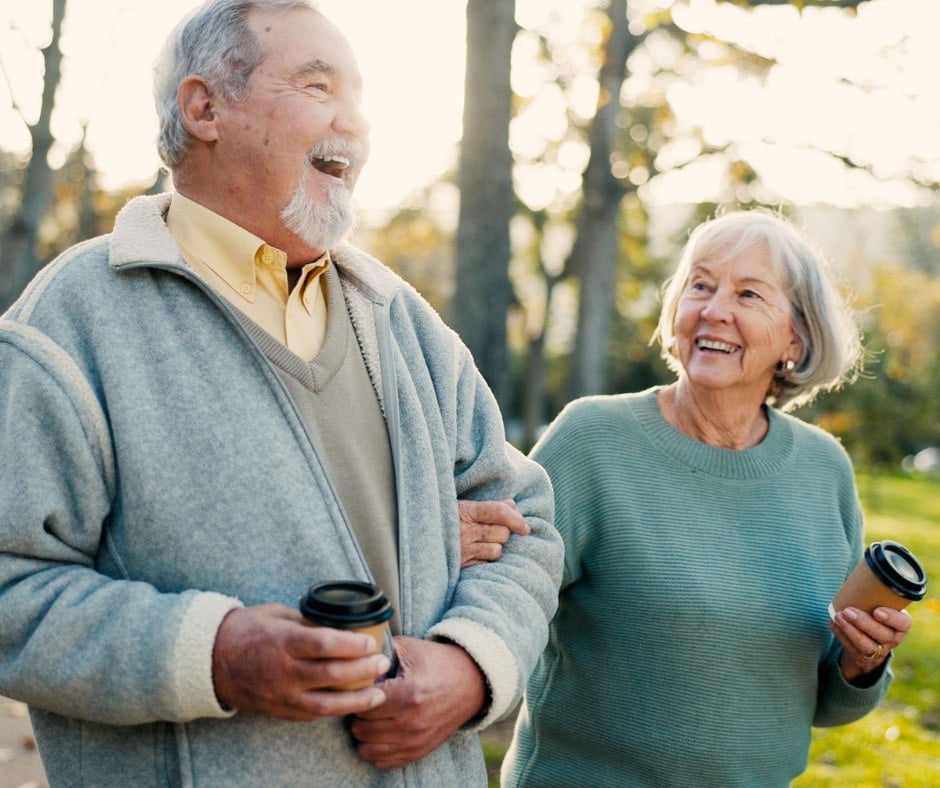 Senior couple walking outdoors with coffee, smiling and enjoying an active, happy lifestyle.
